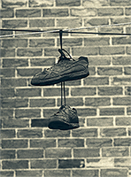 An old pair of black sneakers hanging from an electrical wire in front of a brick wall
