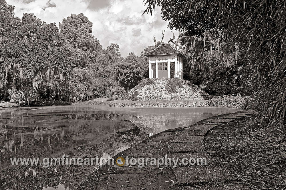a calm water pond with a white Buddhist temple and a stone path leading away with trees and clouds