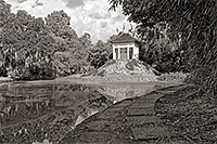 a calm water pond with a white Buddhist temple and a stone path leading away with trees and clouds