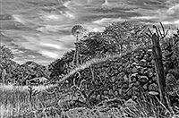 a rock wall leading to an old wind mill water pump on a rustic farm in arizona